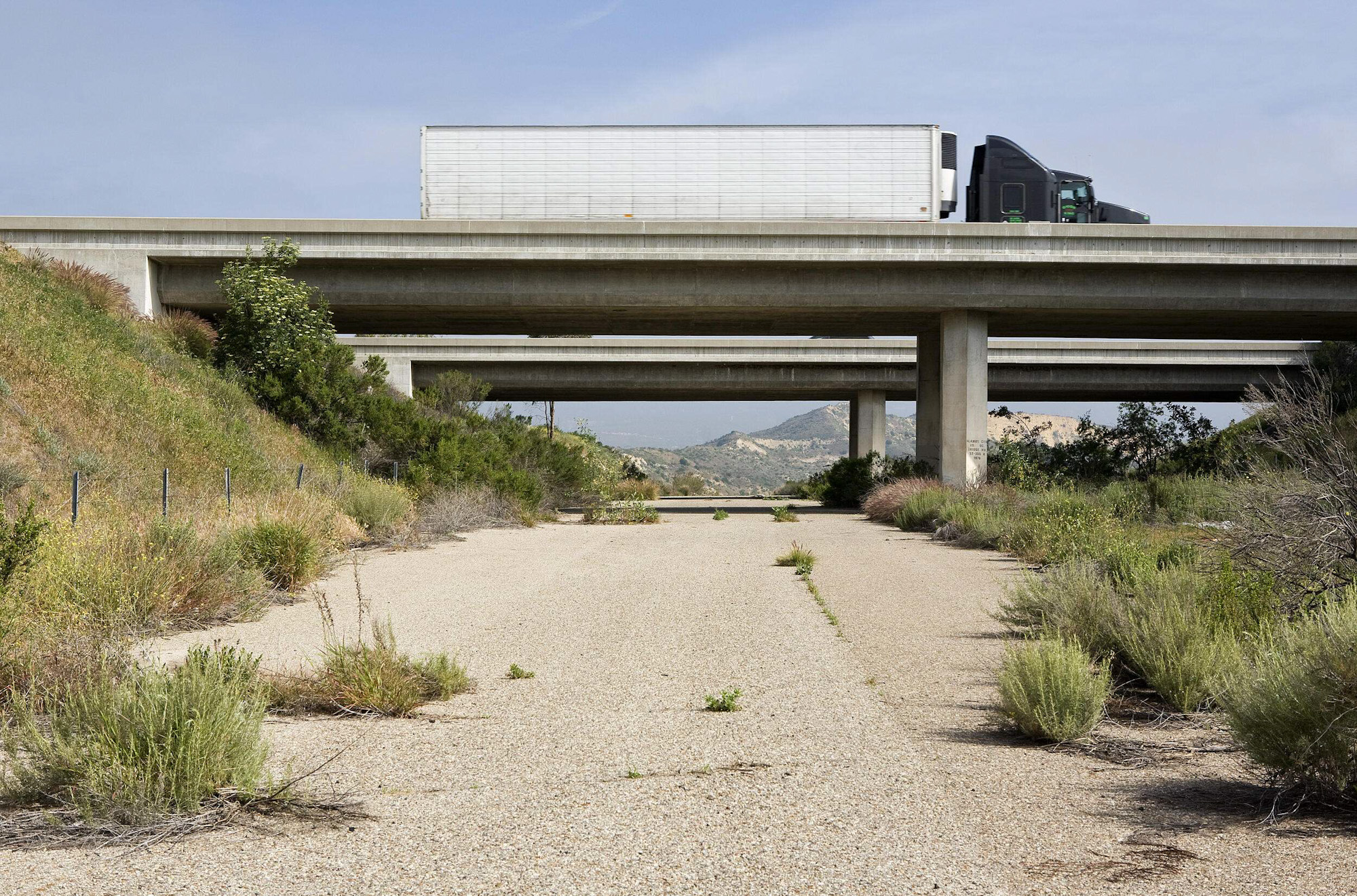 A road passes under a set of highway overpasses, one of which is being crossed by a semi truck.